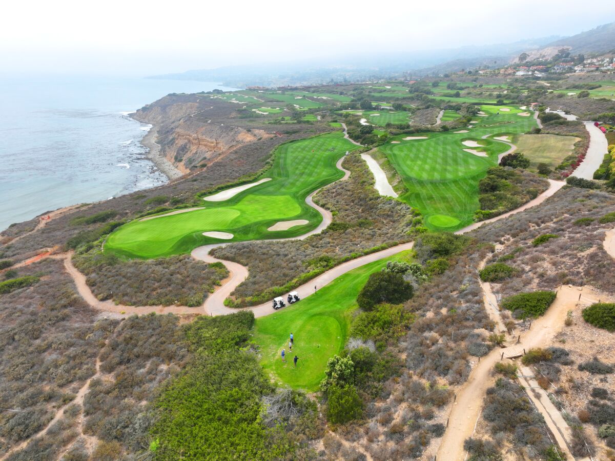 A bird's-eye view of a golf course with bright green patches amid dry, brown vegetation.