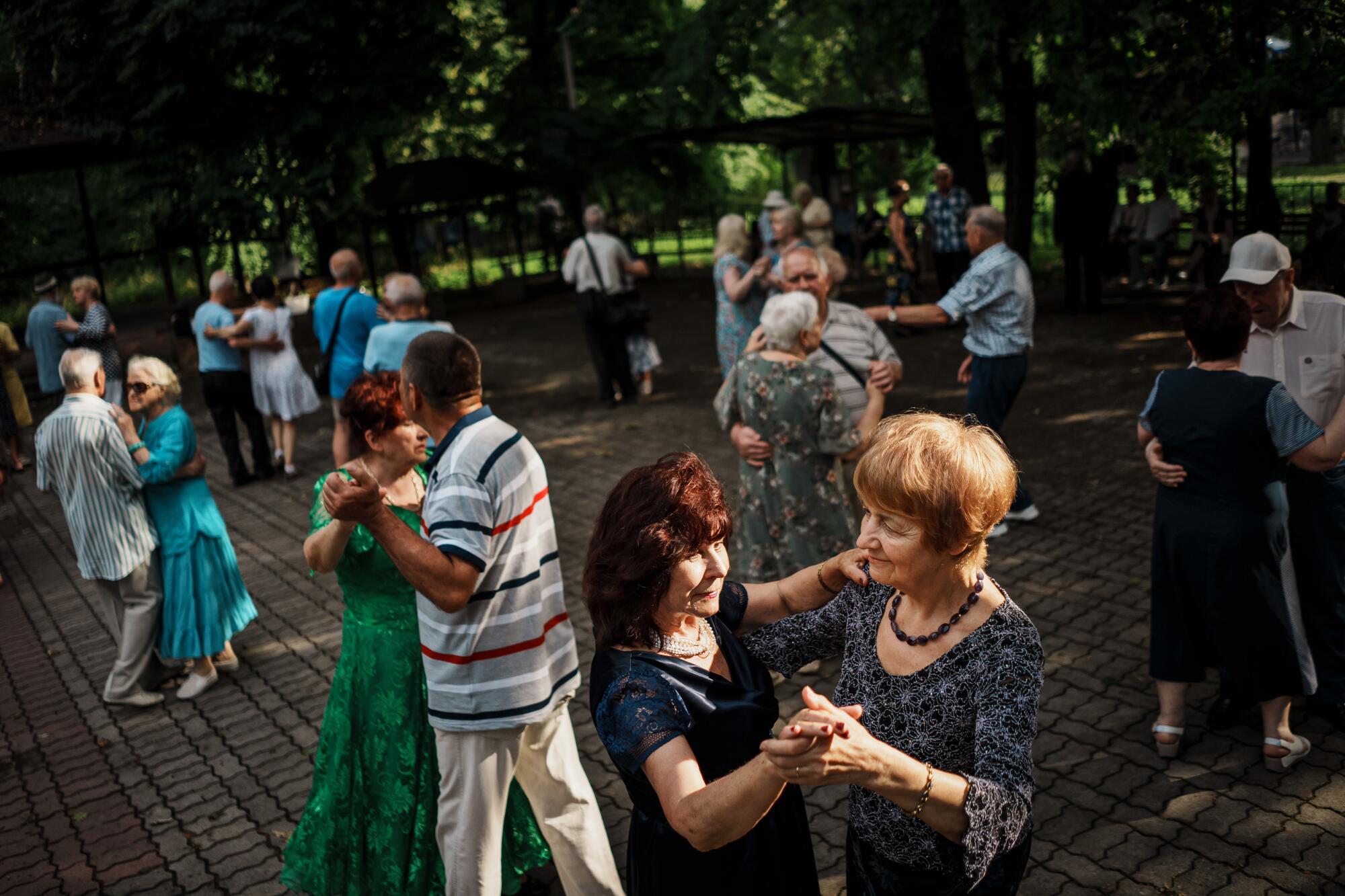 Couples dance in a park with trees in the background 