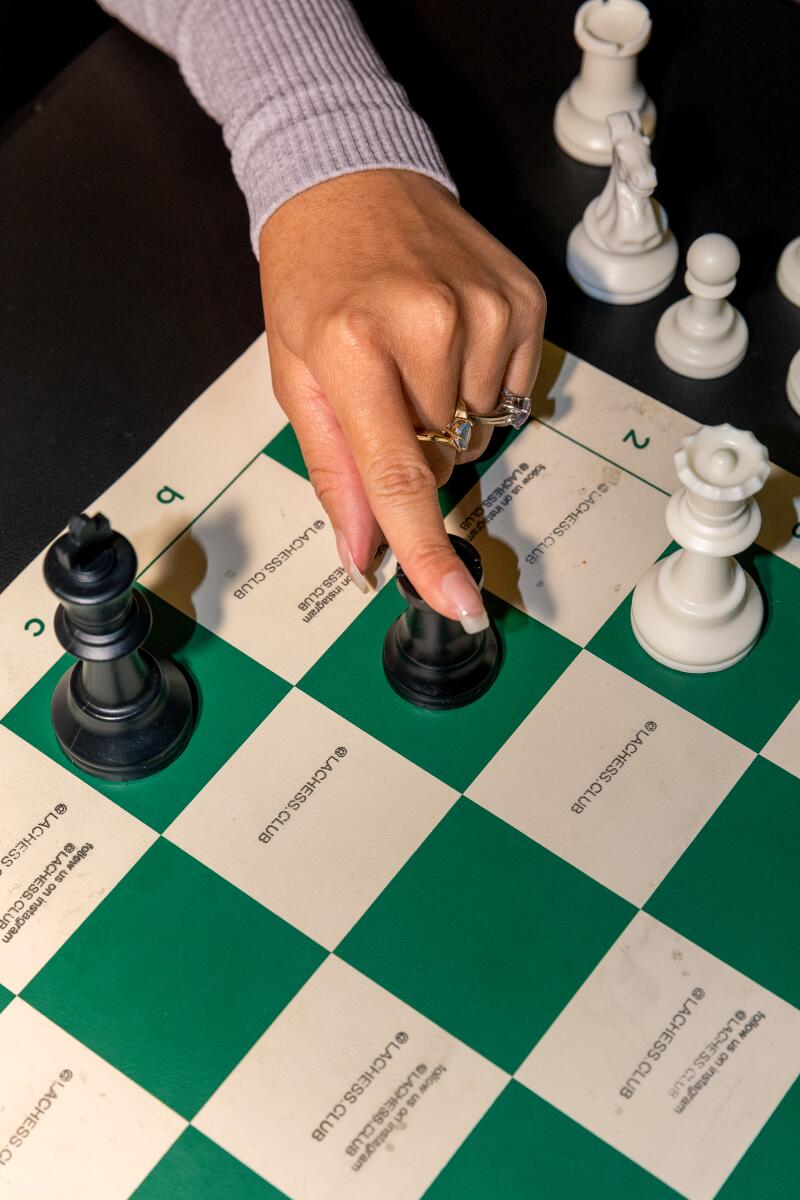 A closeup of a hand moving a chess piece on a green and white chess board.