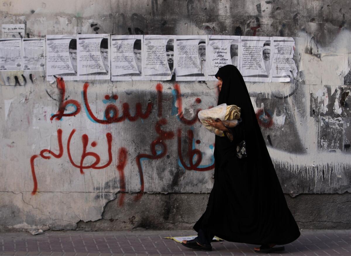 A woman passes a wall on March 24, 2011, in Karkazan, Bahrain, where graffiti reads “our demand is the fall of the unjust regime.”