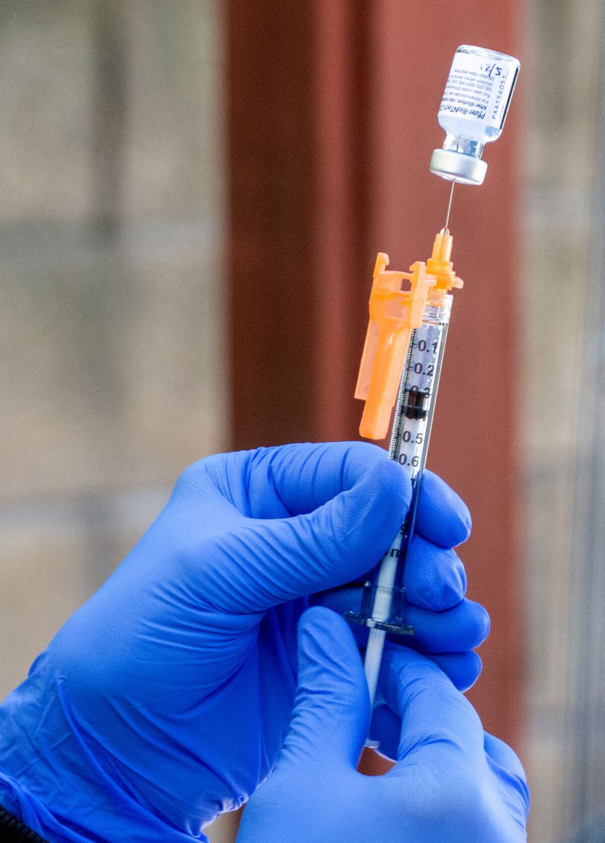 Two hands hold up a needle inserted into a vial.