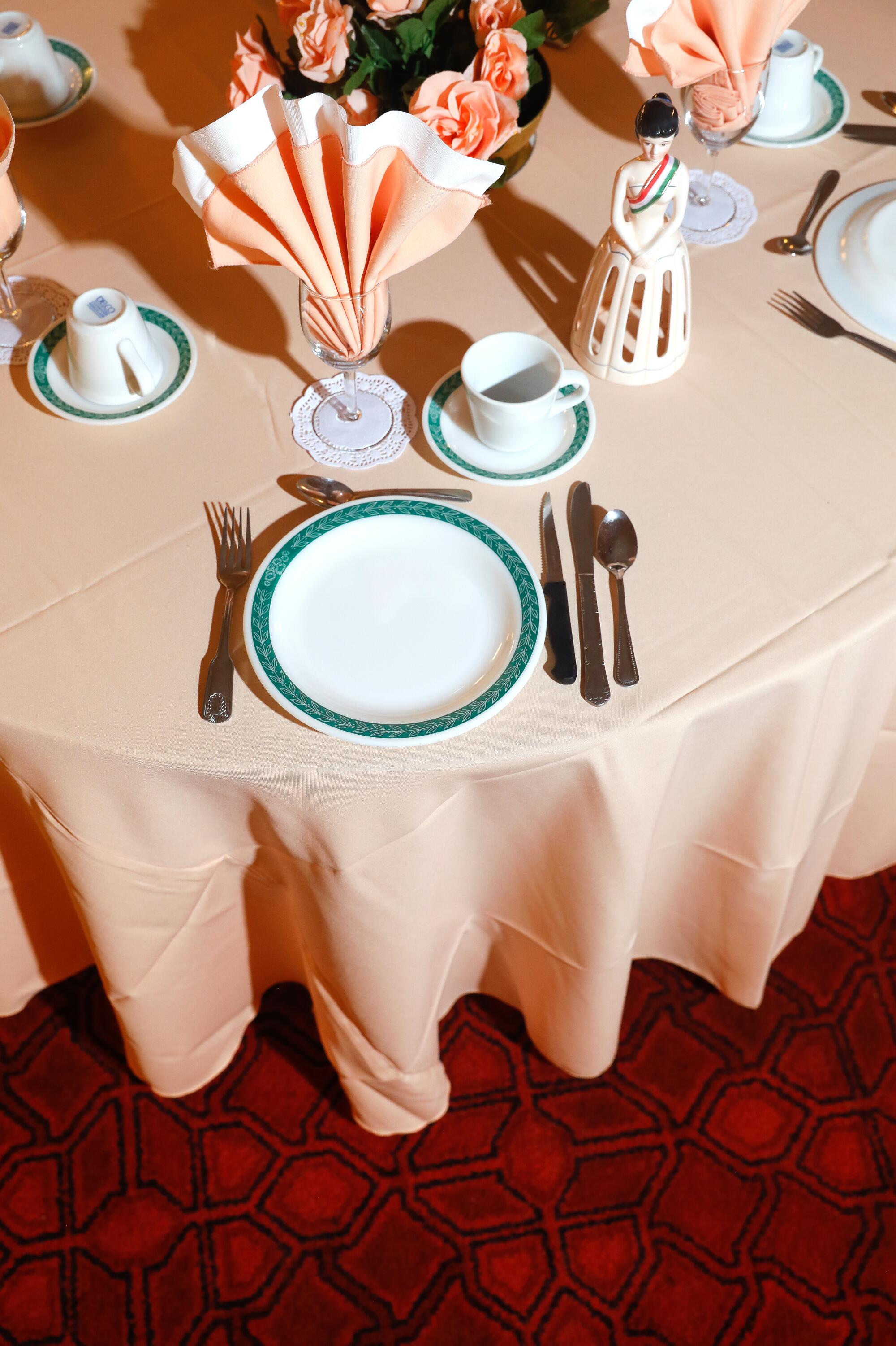 White plates with a green rim, cutlery, a pink tablecloth and pink napkins decorate a table.