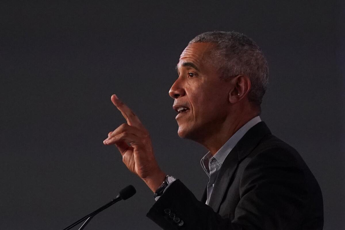 Former President Obama holds up his hand and talks in a microphone