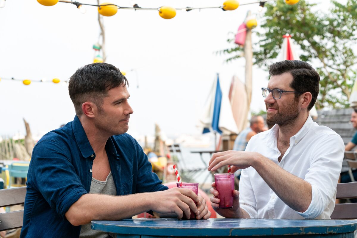 Luke Macfarlane and Billy Eichner look at each other with drinks in hand.