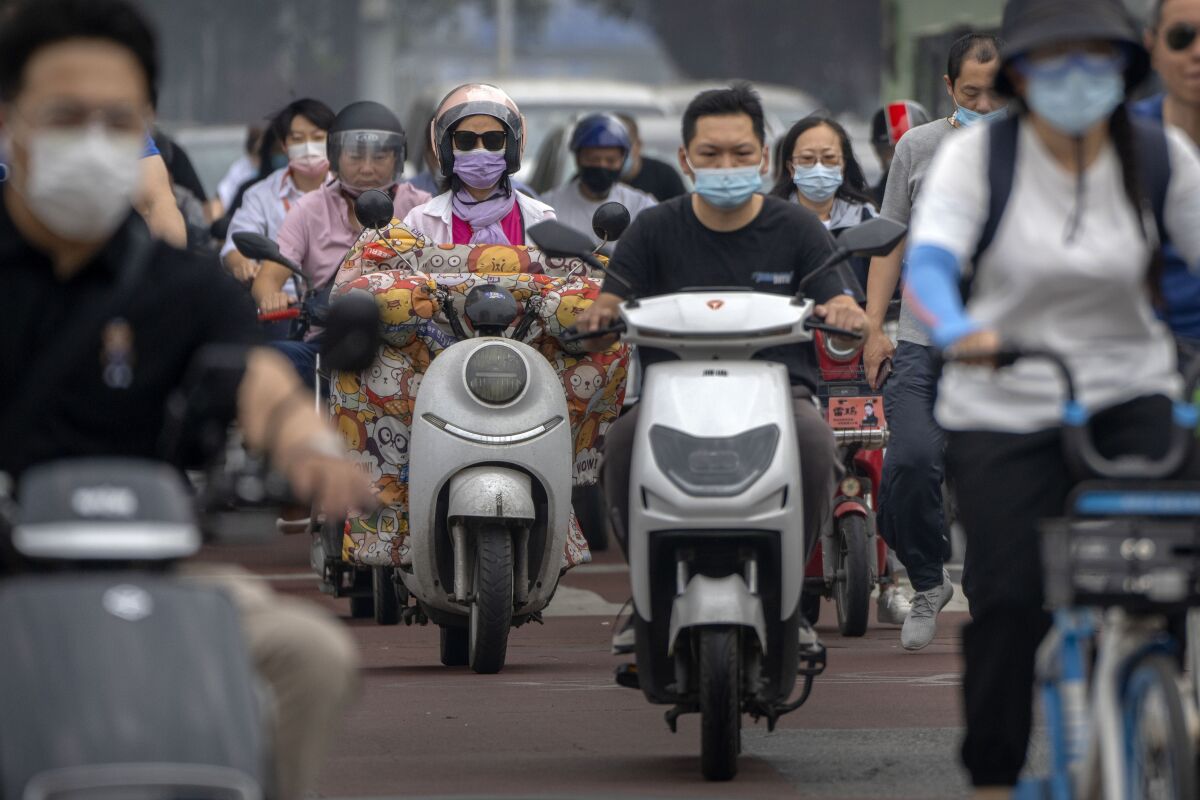Commuters wearing face masks ride across an intersection in the central business district in Beijing, Friday, June 17, 2022. (AP Photo/Mark Schiefelbein)