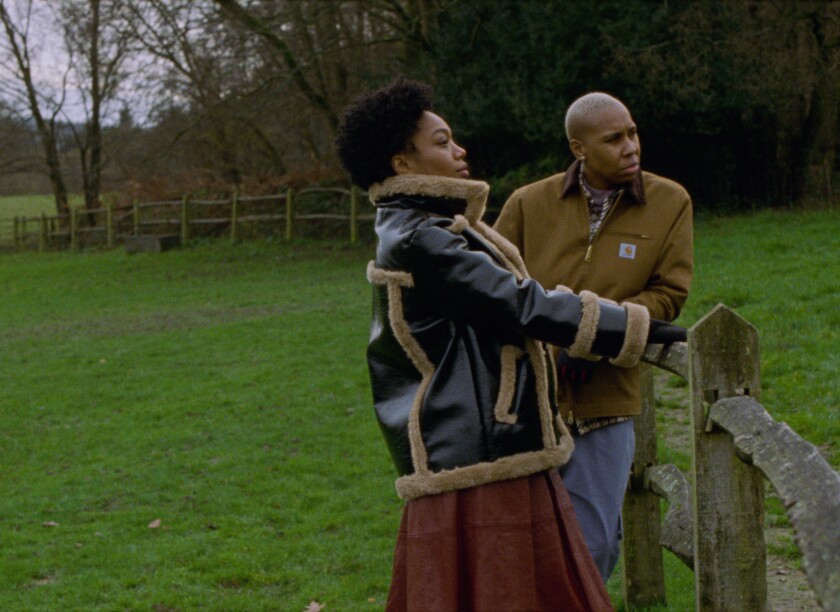 Two women in outerwear stand by a fence in a field