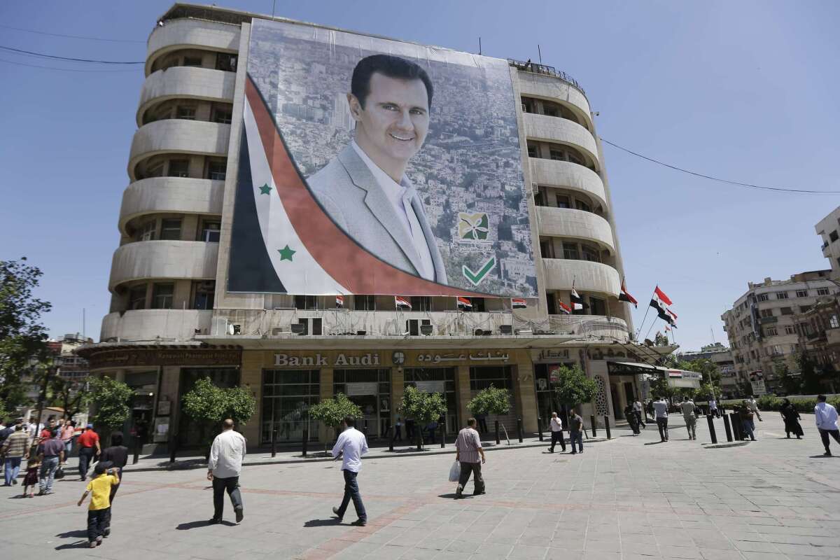 Syrians walk past a giant campaign billboard of Syrian President Bashar Assad on Sunday in the capital of Damascus.