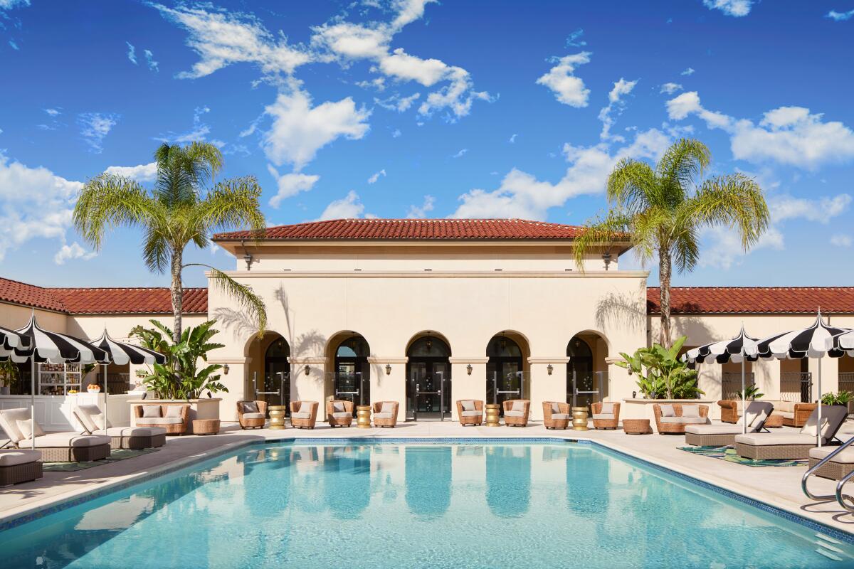 A rooftop pool before a red-tile-roofed building with an arcade and palm trees