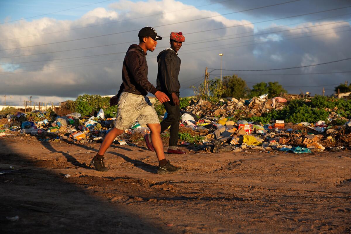 Two men walk past piles of refuse in Makhanda. The trash should have been removed by municipal services. The municipality is one of South Africa's worst managed.