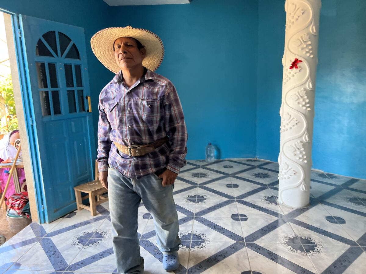 Geniş kenarlı şapkalı bir adam açık maviye boyanmış bir odada duruyor. 