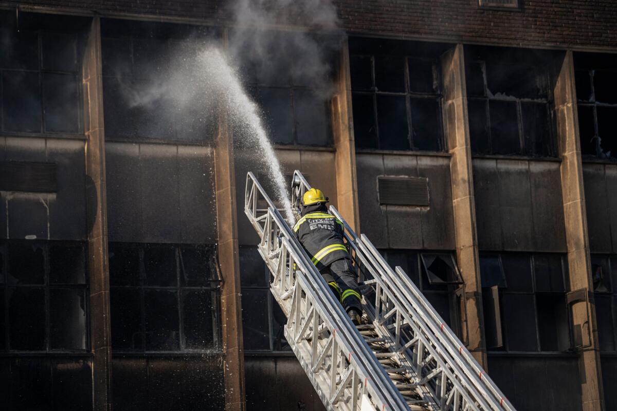 A firefighter on a ladder aims a fire hose into a smoke-filled window