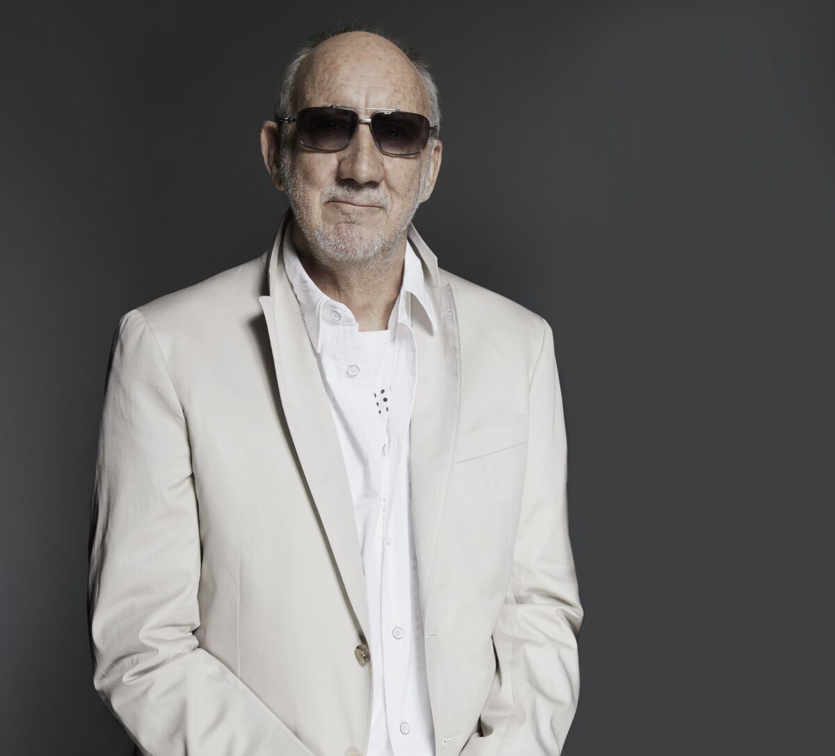 Pete Townshend in a white shirt, cream blazer and dark glasses.