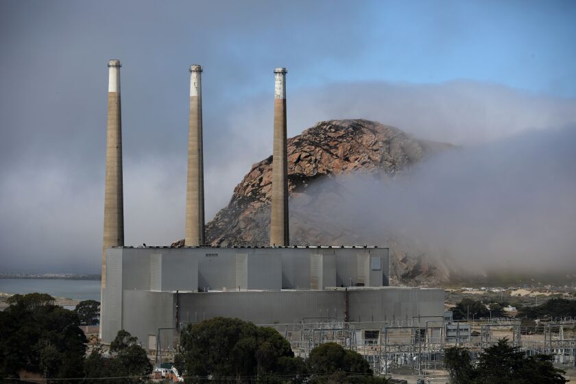 MORRO BAY, CA - AUGUST 03: Three smokestacks from the old power plant, which closed permanently in 2014, are set to come down by January 1, 2028, Morro Rock shown in the background, on Wednesday, Aug. 3, 2022 in Morro Bay, CA. Three 450-foot smokestacks that have become icons in Morro Bay - along with its namesake Morro Rock - are coming down soon because their power plant has closed. The smokestacks, which gave the town its nickname Three Stacks and a Rock, are part of the town's skyline. (Gary Coronado / Los Angeles Times)