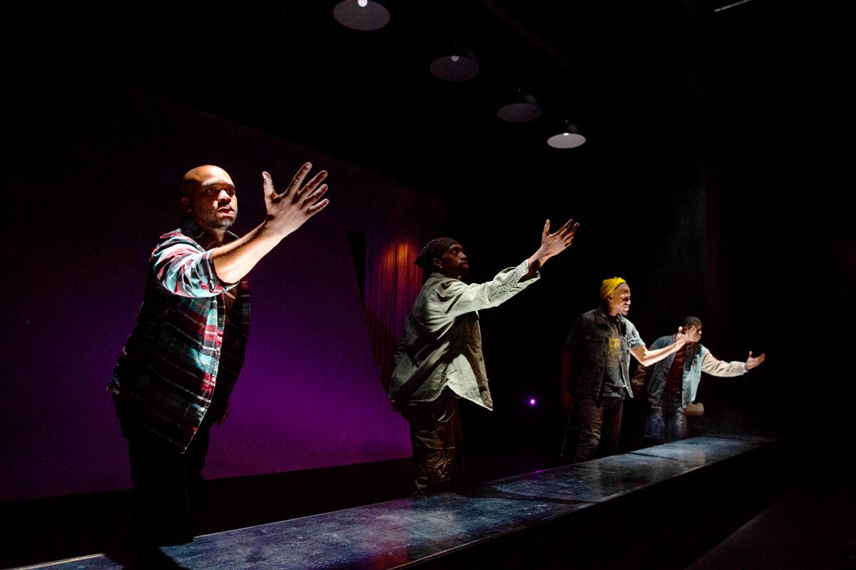 Four men on stage reach out toward the audience in unison