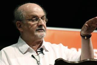 A balding man with a gray goatee and glasses gestures with his left hand while speaking to an unseen audience