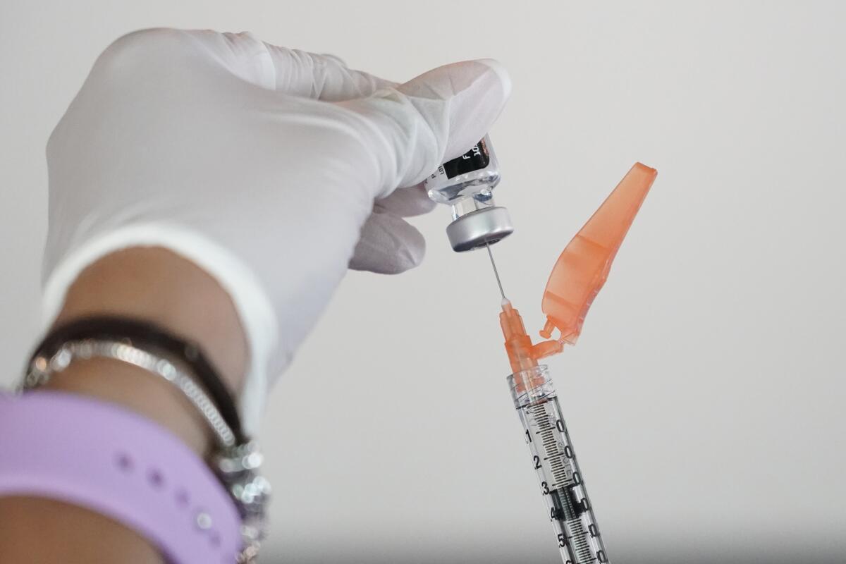Closeup of a syringe being filled from a vial held by a gloved hand.