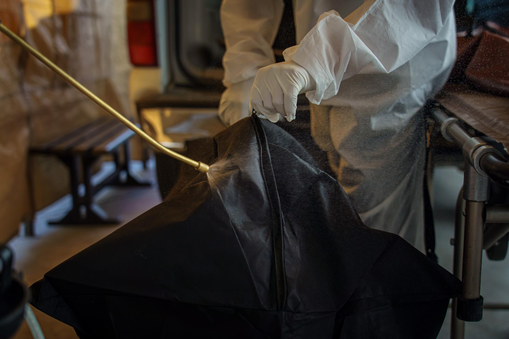 At the San Ramon Funeral Home, workers follow a new protocol for disinfecting corpses as they transfer a person who died from COVID-19 symptoms into a casket.