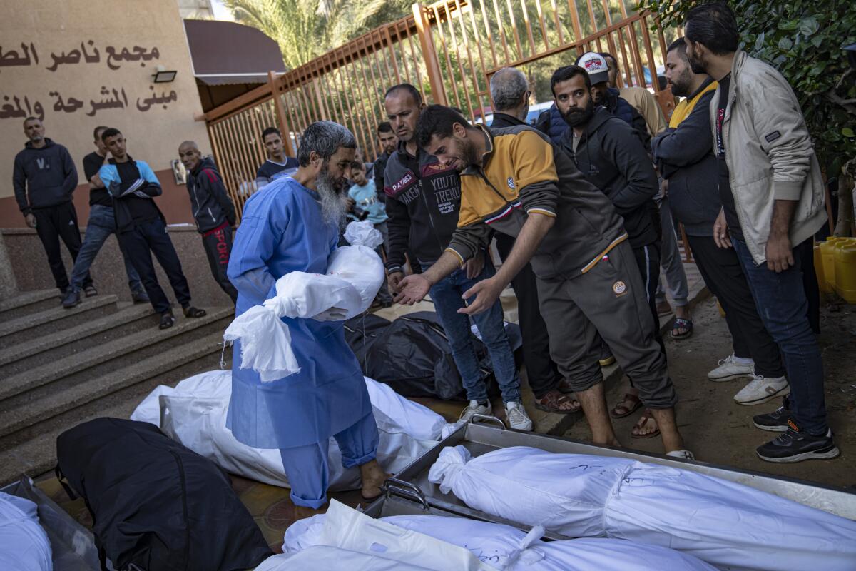 Amid a collection of wrapped bodies, a man hands a small wrapped body to another man