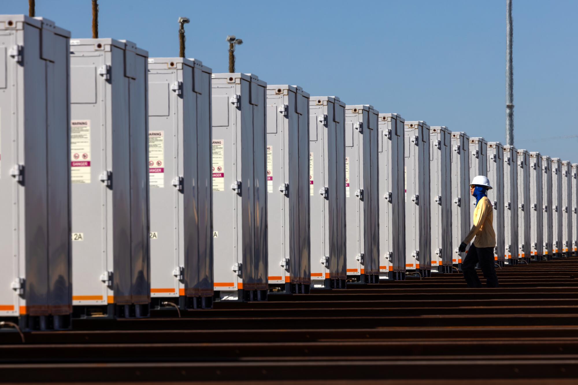 A worker in a hardhat inspects a row of large storage batteries.