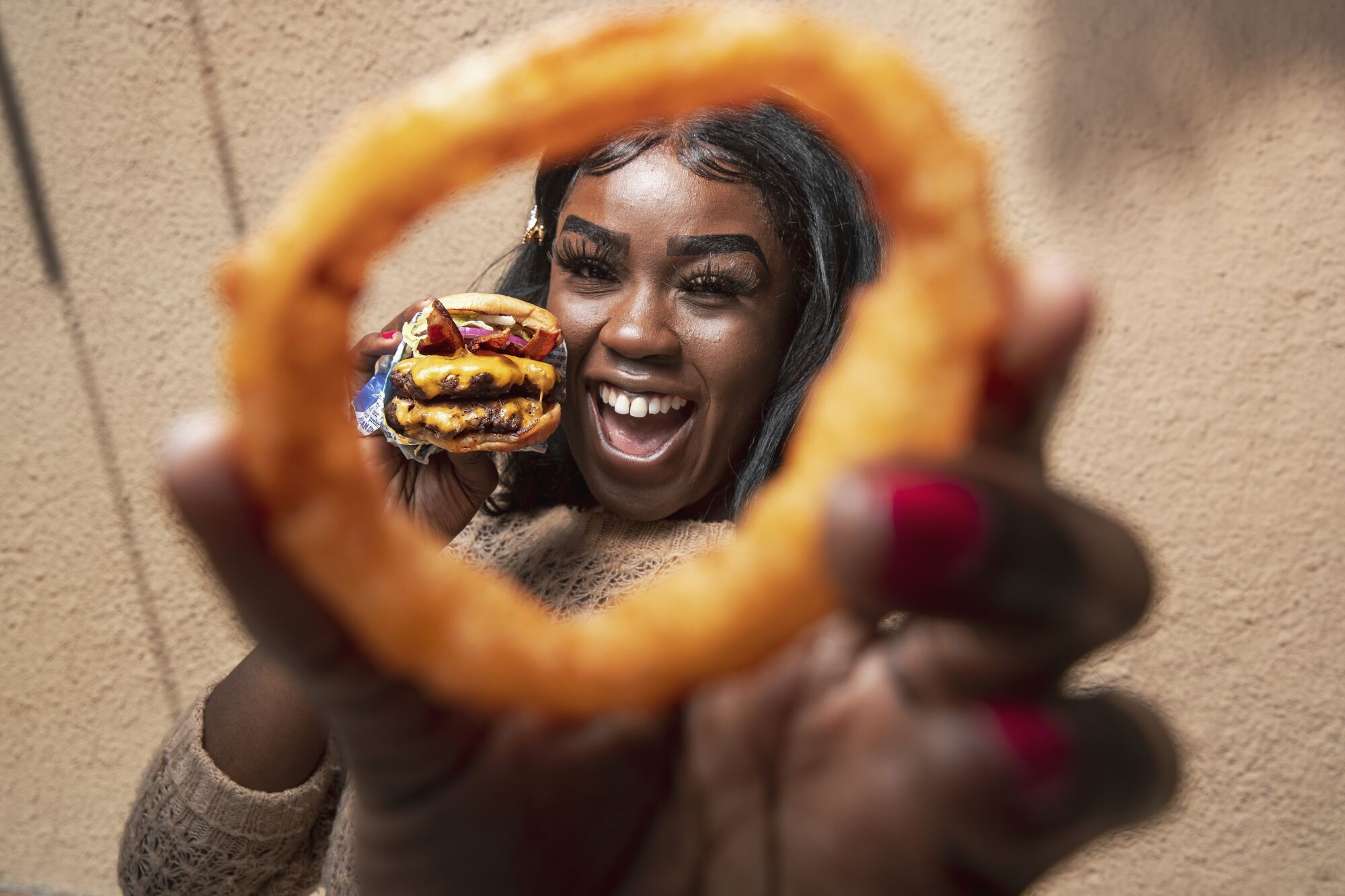 Nkechi Ahaiwe holds an onion ring and a Double VIP Cheeseburger