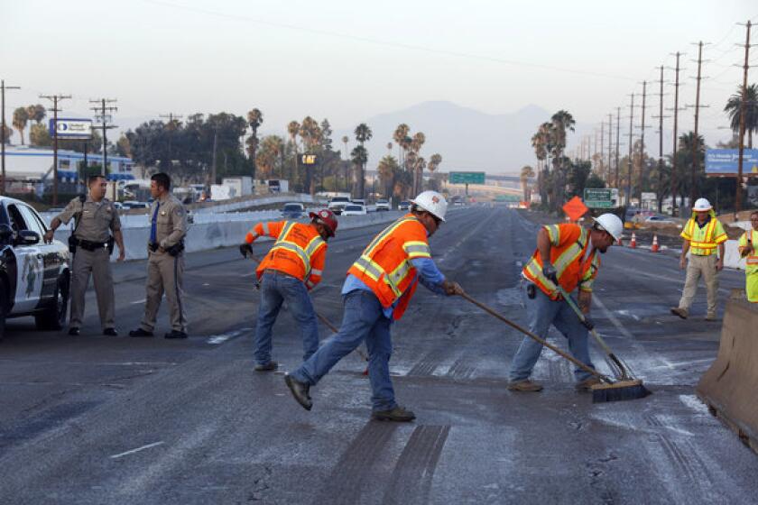 Workers sweep the pavement on a section of the 215 Freeway near Riverside that was closed Friday morning after a construction crew ruptured a gas line.