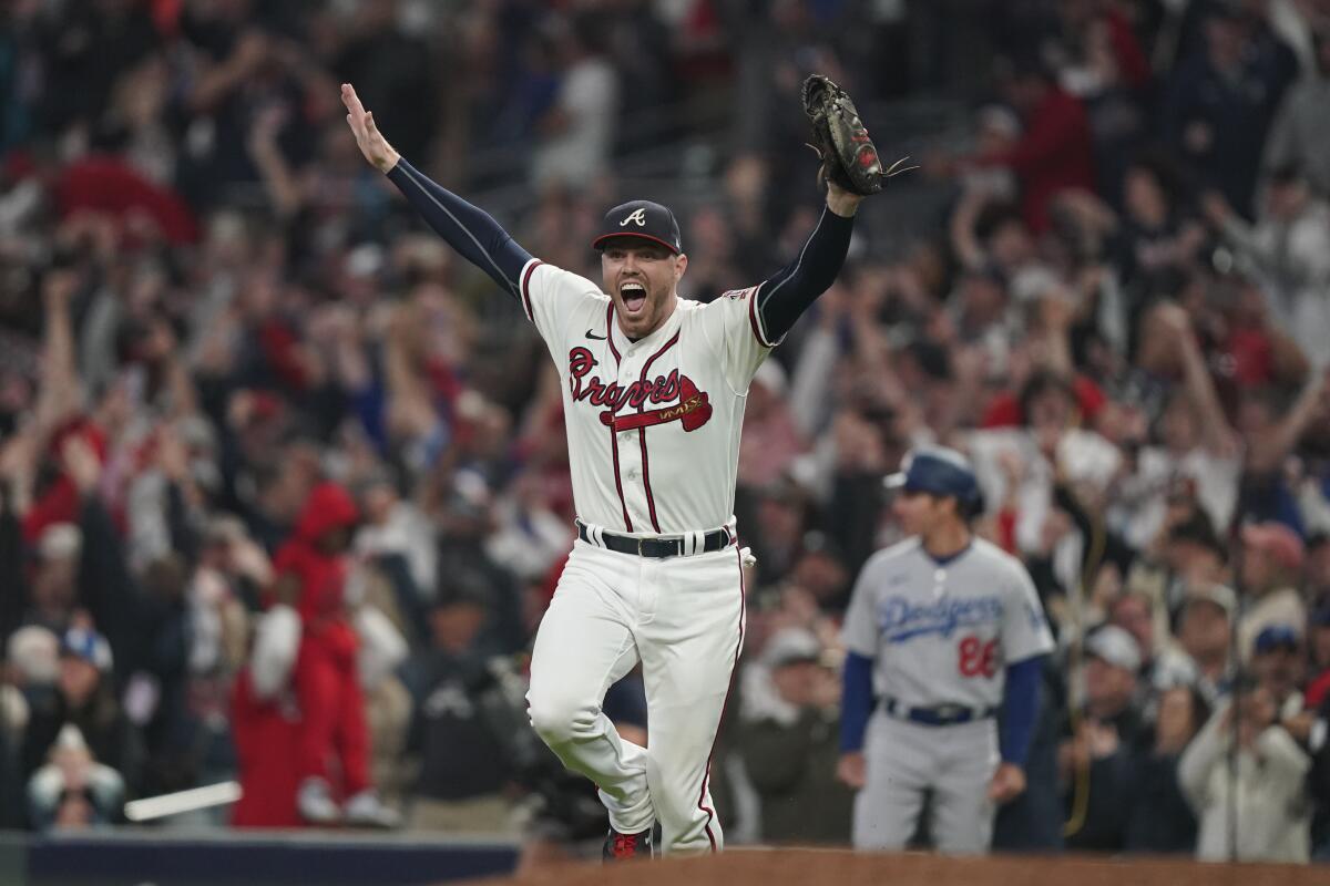 A man in a Braves uniform raises his hands and smiles on the field while fans are in the stands in the background