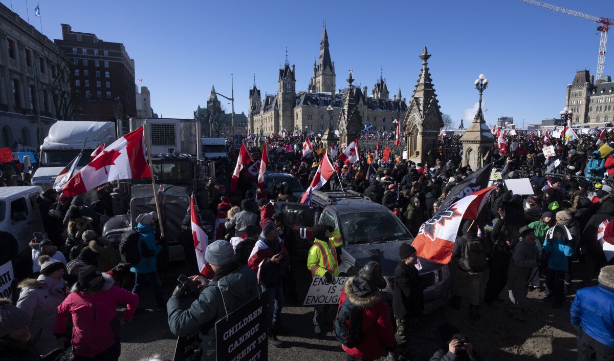 People holding Canadian flags crowd a city street.