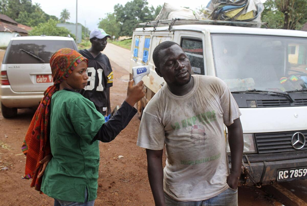 A health worker looking for signs of Ebola checks a man's temperature at a roadblock run by Guinean security forces outside the town of Forecariah, Guinea.
