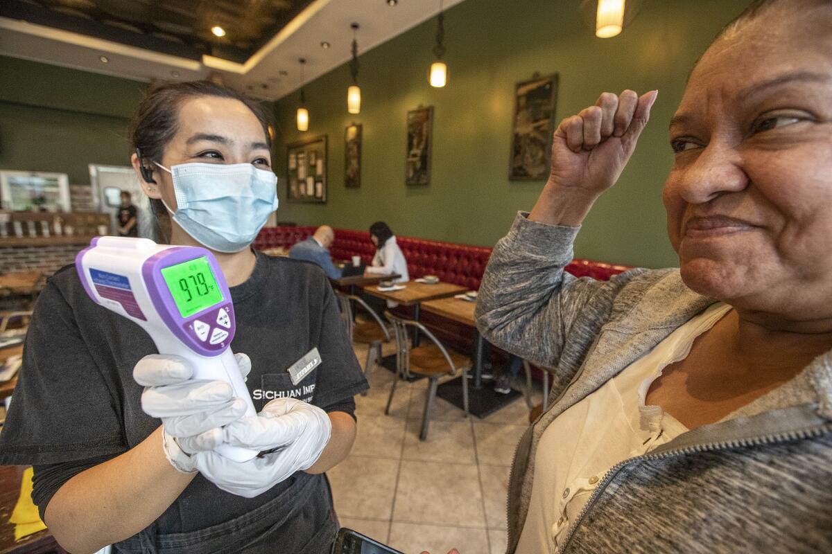 Grace Magallon, 63, right, of East Los Angeles, reacts after having her temperature taken by Sophia Huang, a supervisor at Sichuan Impression restaurant in Alhambra. Amid the continuing coronavirus outbreak, the restaurant, since the end of January, has been using an infrared thermometer, which can take a person's temperature without touching them, to screen patrons. If a customer's temperature is 99.9 or above, they are asked to leave. Magallon's reading was 97.9.