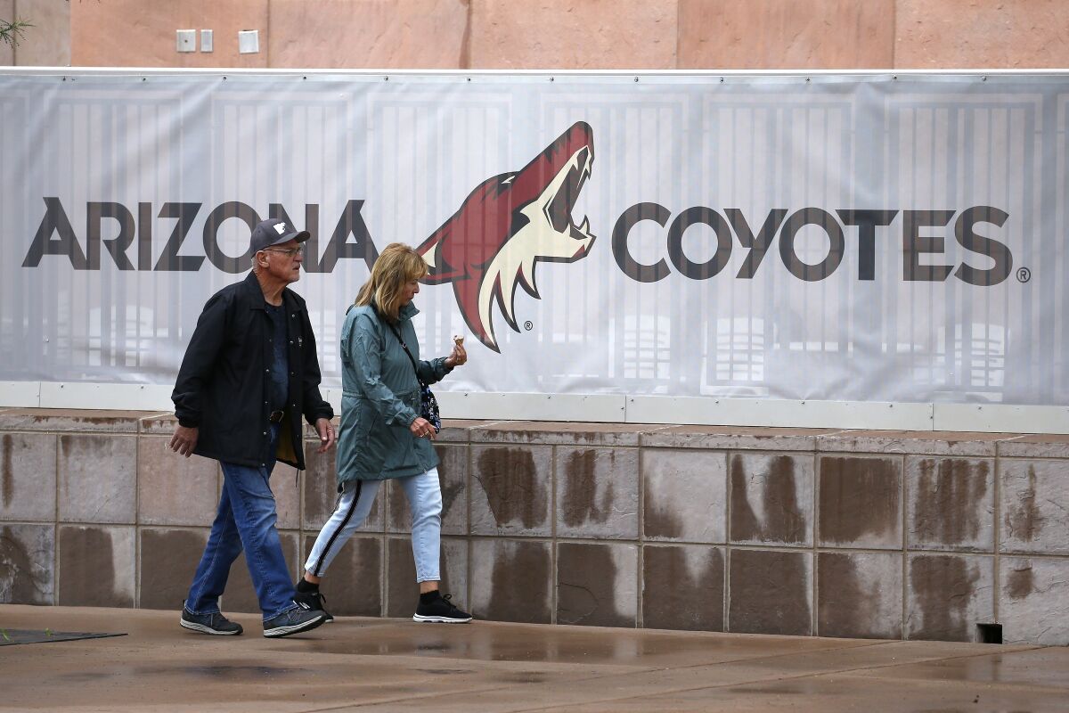 FILE - A couple walks past the Gila River Arena, home of the Arizona Coyotes NHL hockey club, March 12, 2020, in Glendale, Ariz. The Coyotes are all caught up on their bills. No eviction necessary. The hockey team in the desert paid off its overdue bills on Thursday, Dec. 9, 2021, a day after receiving word that the City of Glendale was going to lock them out of their arena if they didn't get caught up. Glendale city manager Kevin Phelps sent a letter on Wednesday informing the Coyotes they owe $1.3 million, including $250,000 to the city. (AP Photo/Ross D. Franklin, file)