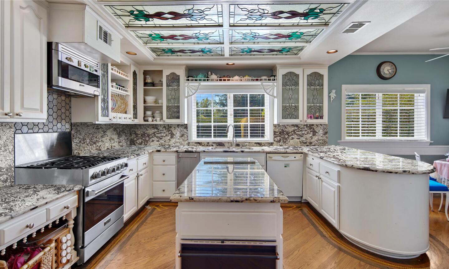The kitchen has white cabinets and an island and wooden floor.