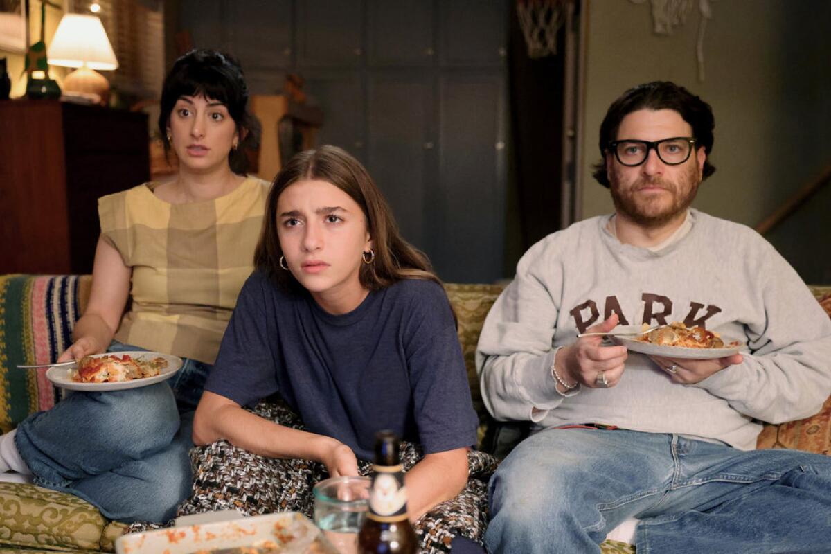 A woman, a teenage girl and a man sitting on a sofa watching television.