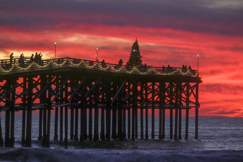 People take photos of Crystal Pier, with a Christmas tree at the end of it, at sunset in Pacific Beach on Tuesday, December 10, 2019 in San Diego, California.
