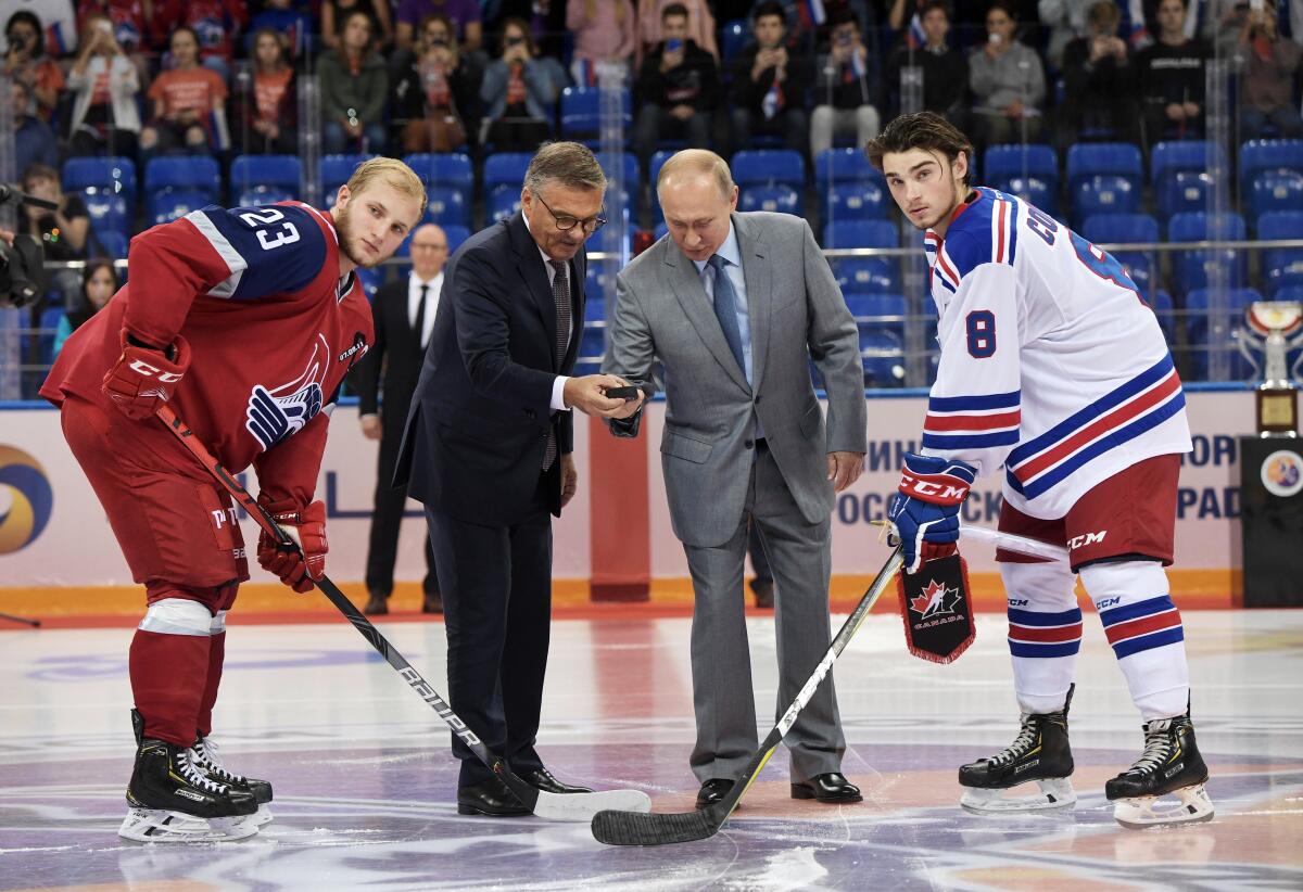Vladimir Putin and International Ice Hockey Federation President Rene Fasel stand on the ice with hockey players