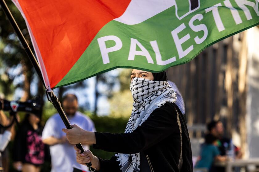 IRVINE, CA - APRIL 29, 2024: A protester carries a Palestinian flag in solidarity with a pro-palestinian encampment nearby in the central part of the UC Irvine campus on April 29, 2024 in Irvine, California.(Gina Ferazzi / Los Angeles Times)