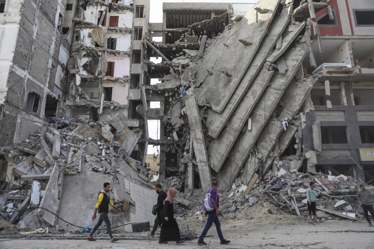 ARCHIVO - Palestinos caminan frente a edificios impactados por ataques israelíes 