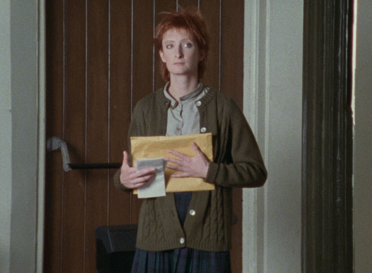 A woman wearing a cardigan holding papers in the movie “I’ve Heard the Mermaids Singing.”