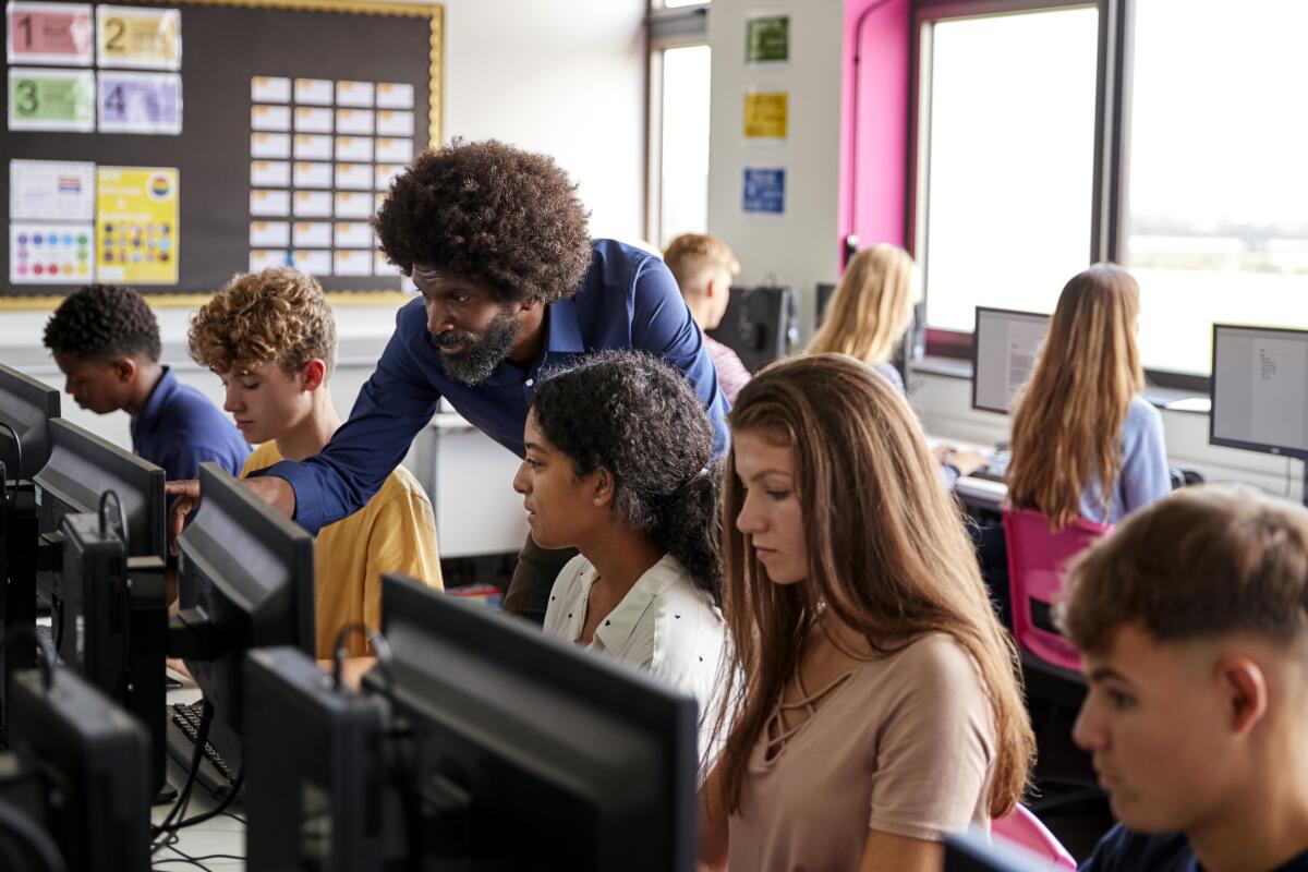 A male teacher helps students in a computer class.
