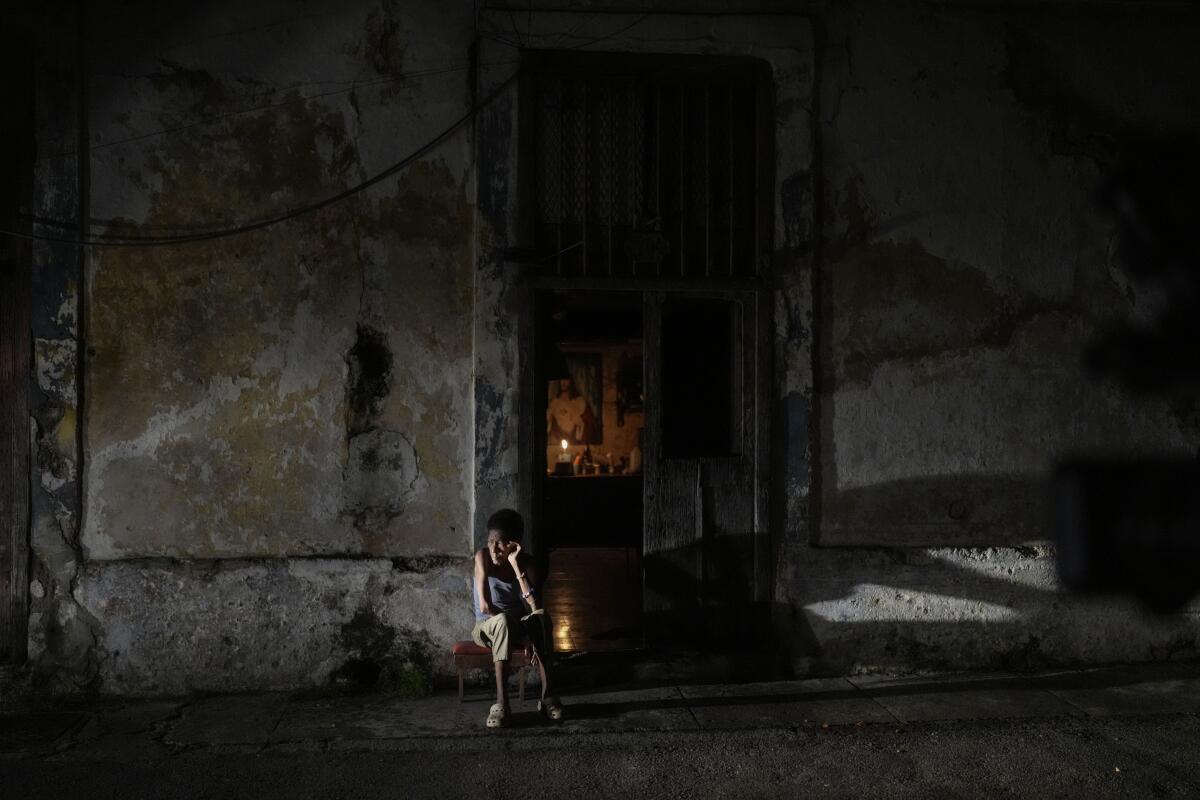 A resident sits outside a building at night while passing time during a blackout.