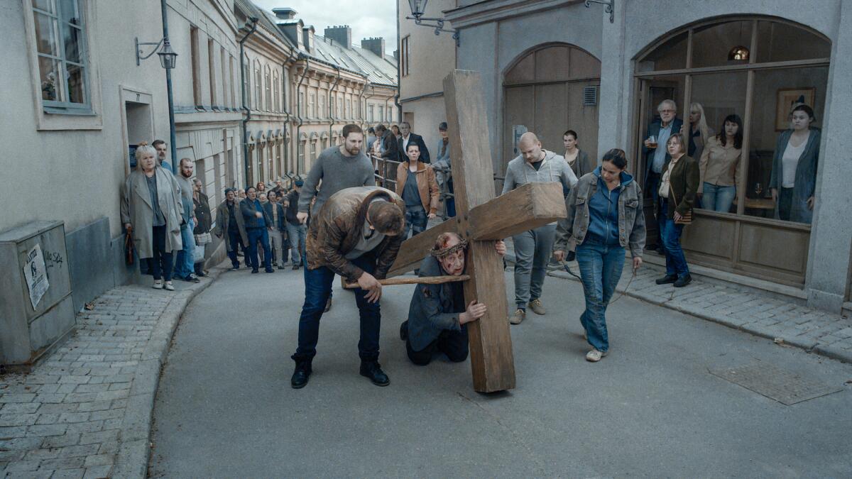 A man carries a cross through a modern street in the movie "About Endlessness."