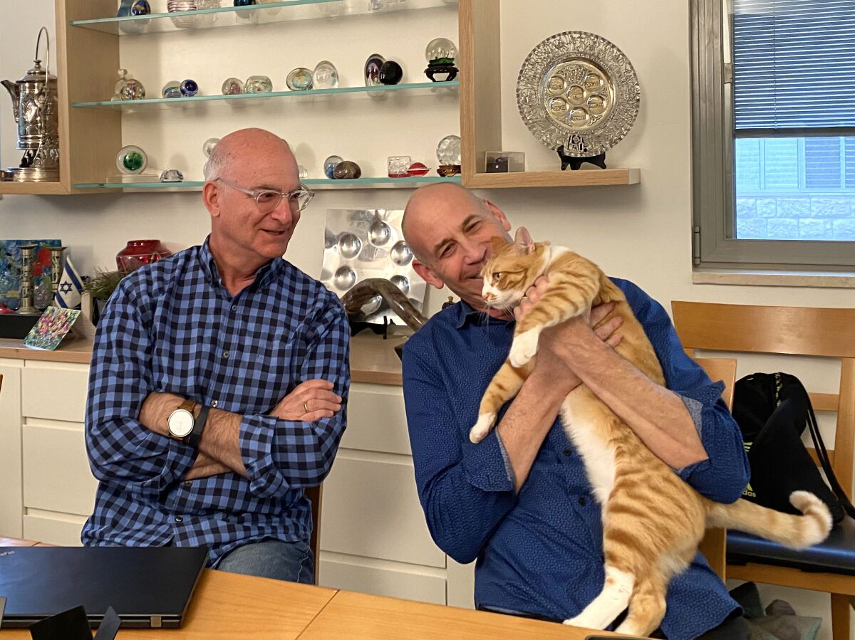 Rabbi Donald Goor, left, and Cantor Evan Kent, in their Jerusalem living room, with their rescue cat, Archie.