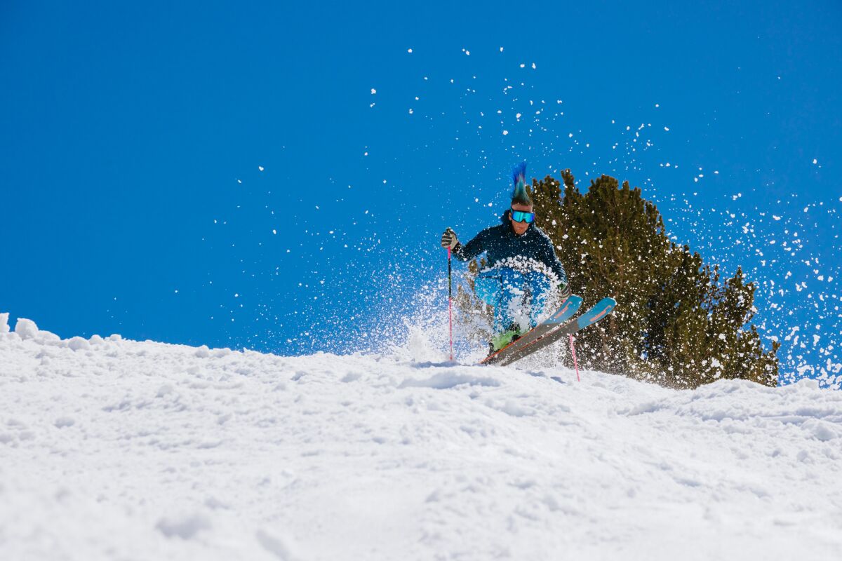 A skier kicks up a flurry of snow as they ride on a clear day