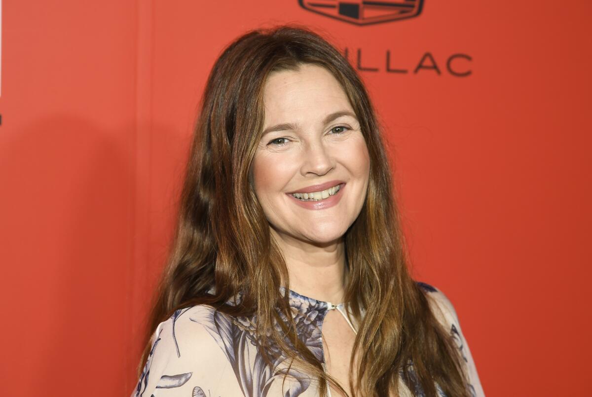 Drew Barrymore smiles against a red backdrop.