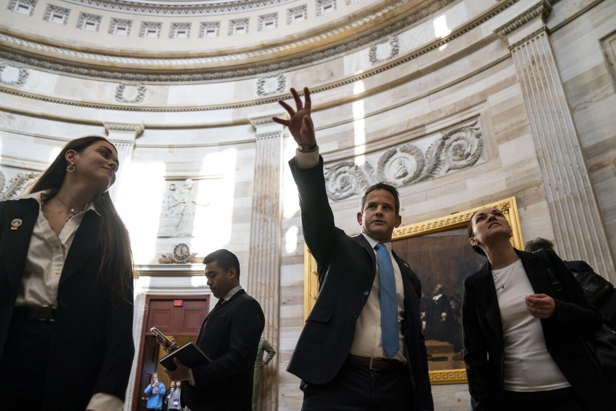 Adam Kinzinger stretching out a hand in an ornate room as others look on