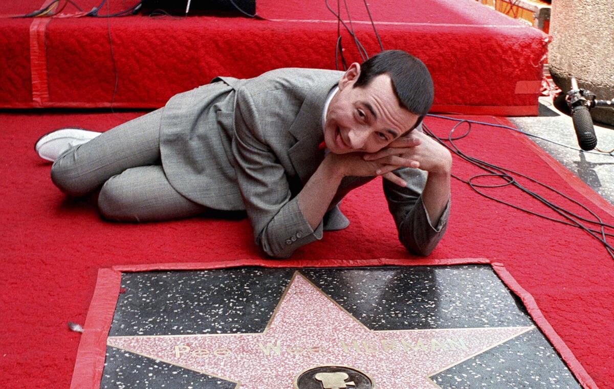 Pee-wee Herman lies on a sidewalk, resting his chin on his hands, and looks thrilled next to his star on the Walk of Fame