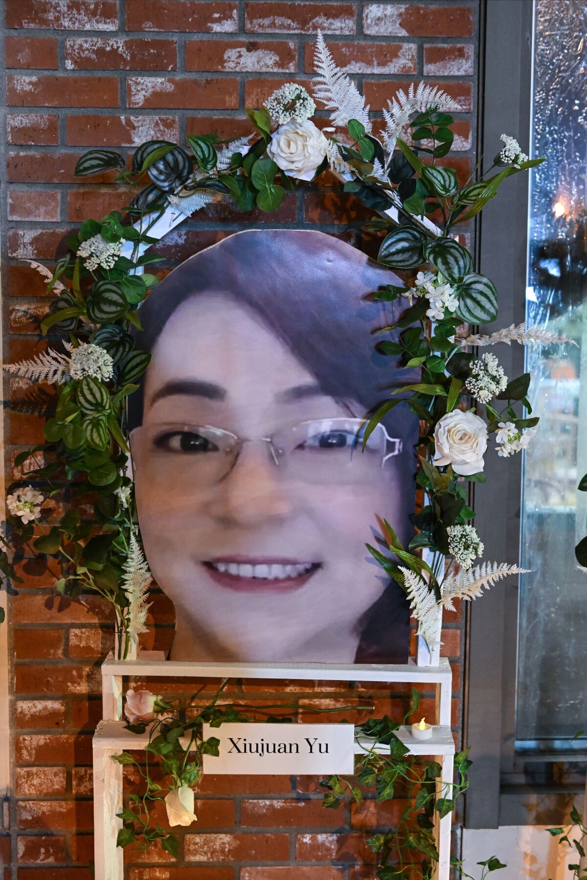 Flowers surround a large portrait of a smiling woman mounted on a brick wall