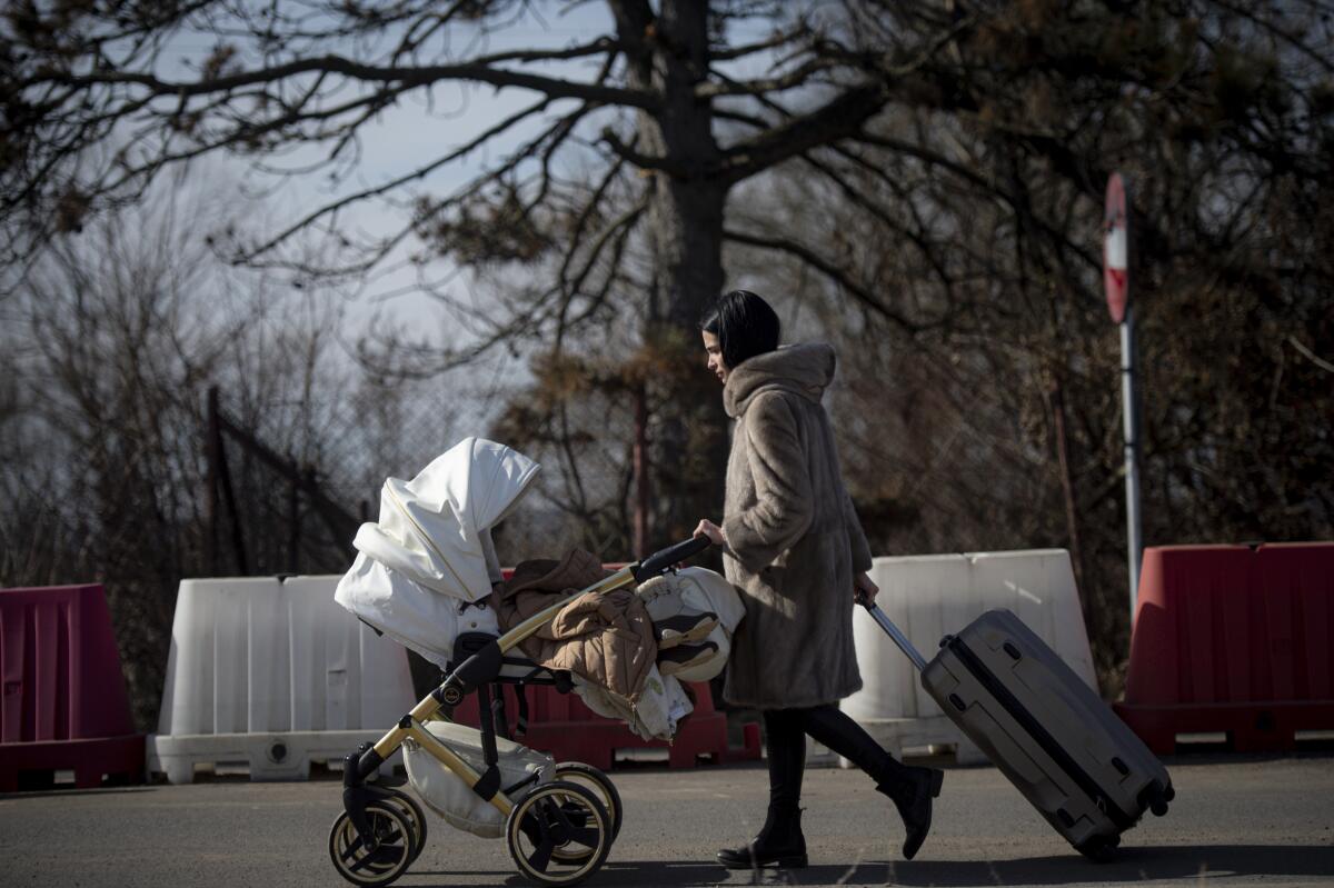 Una mujer con un carrito de bebés y una maleta luego de cruzar la frontera ucraniana en Siret