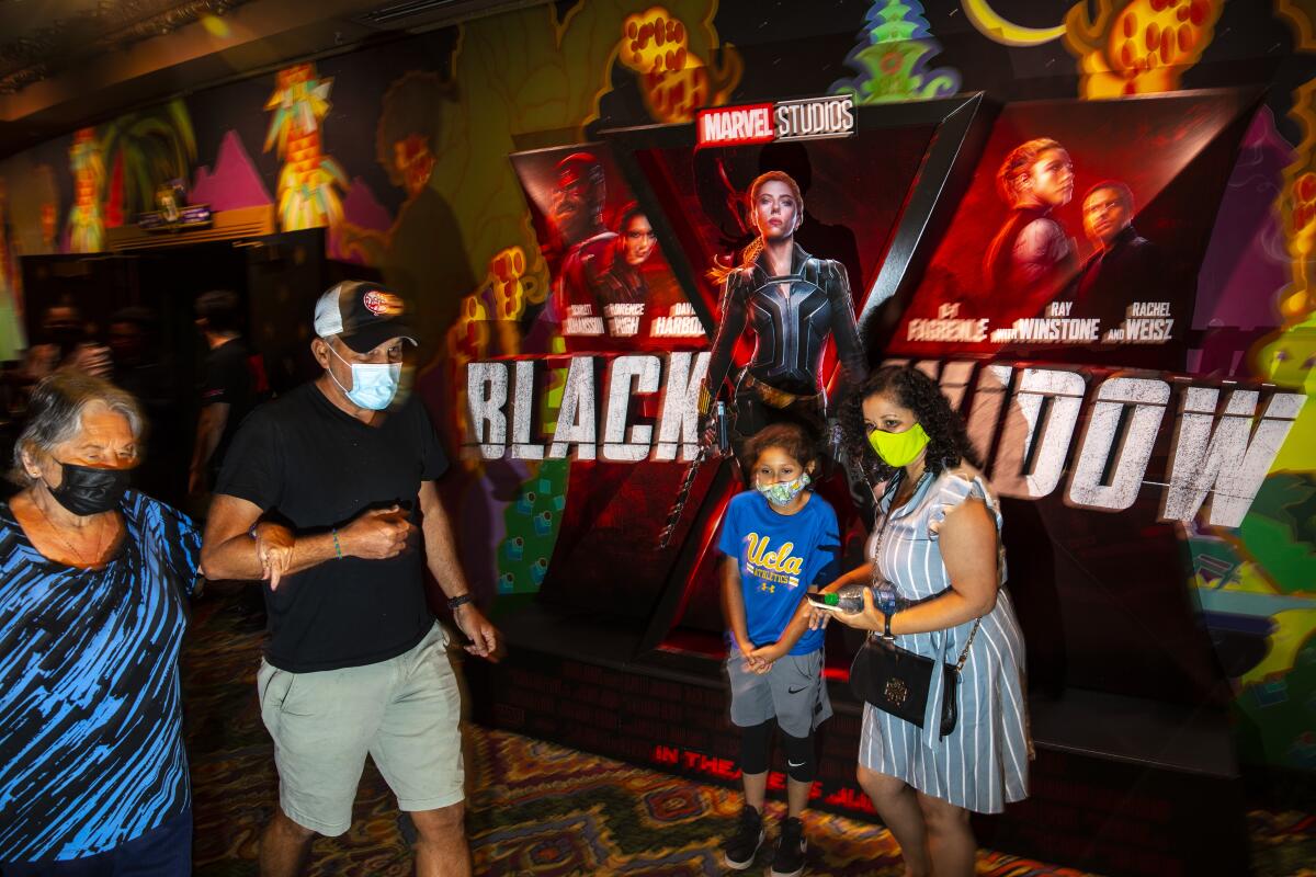 Masked patrons walk past a lobby display for Marvel Studios' "Black Widow," on opening weekend at the El Capitan Theatre