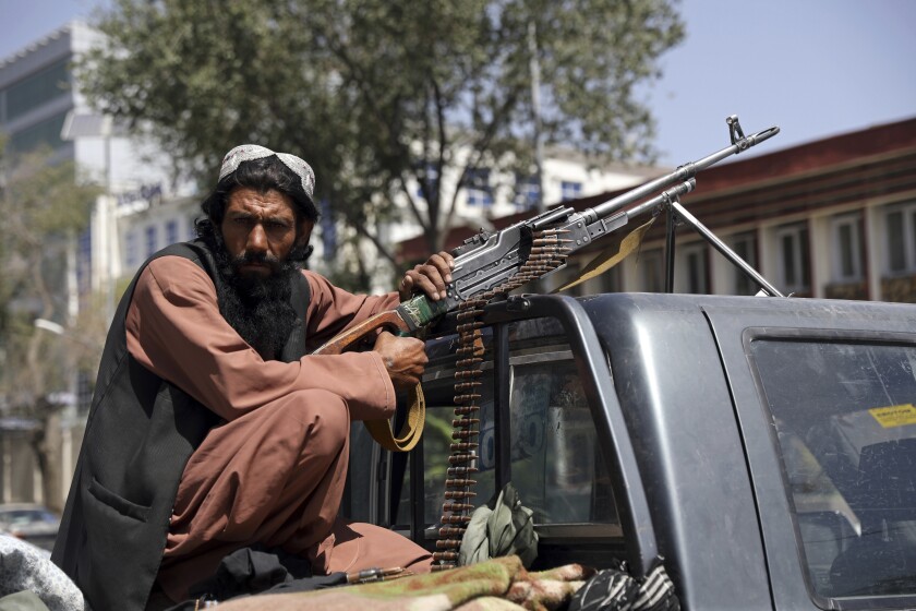 An armed Taliban fighter sits in a truck in front of the main gate leading to the presidential palace in Kabul, Afghanistan.