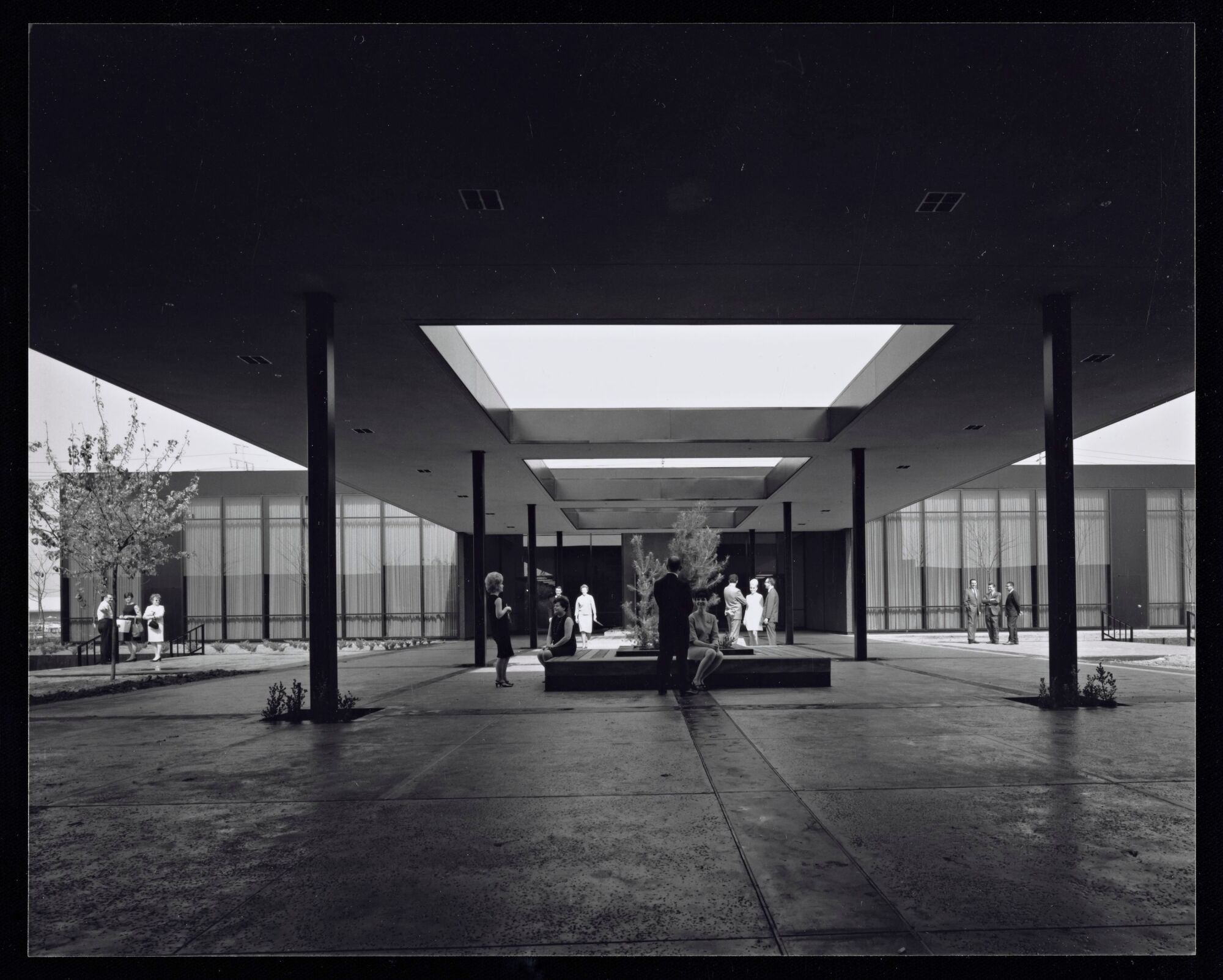 A vintage black and white image shows a covered breezeway with skylight cut out between two buildings